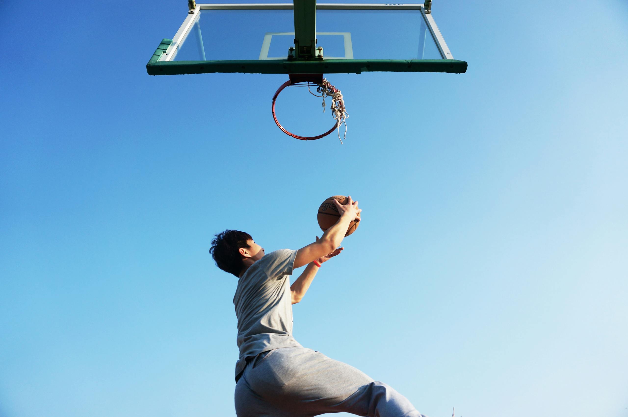 A young man jumping to dunk a basketball outdoors in clear daylight.